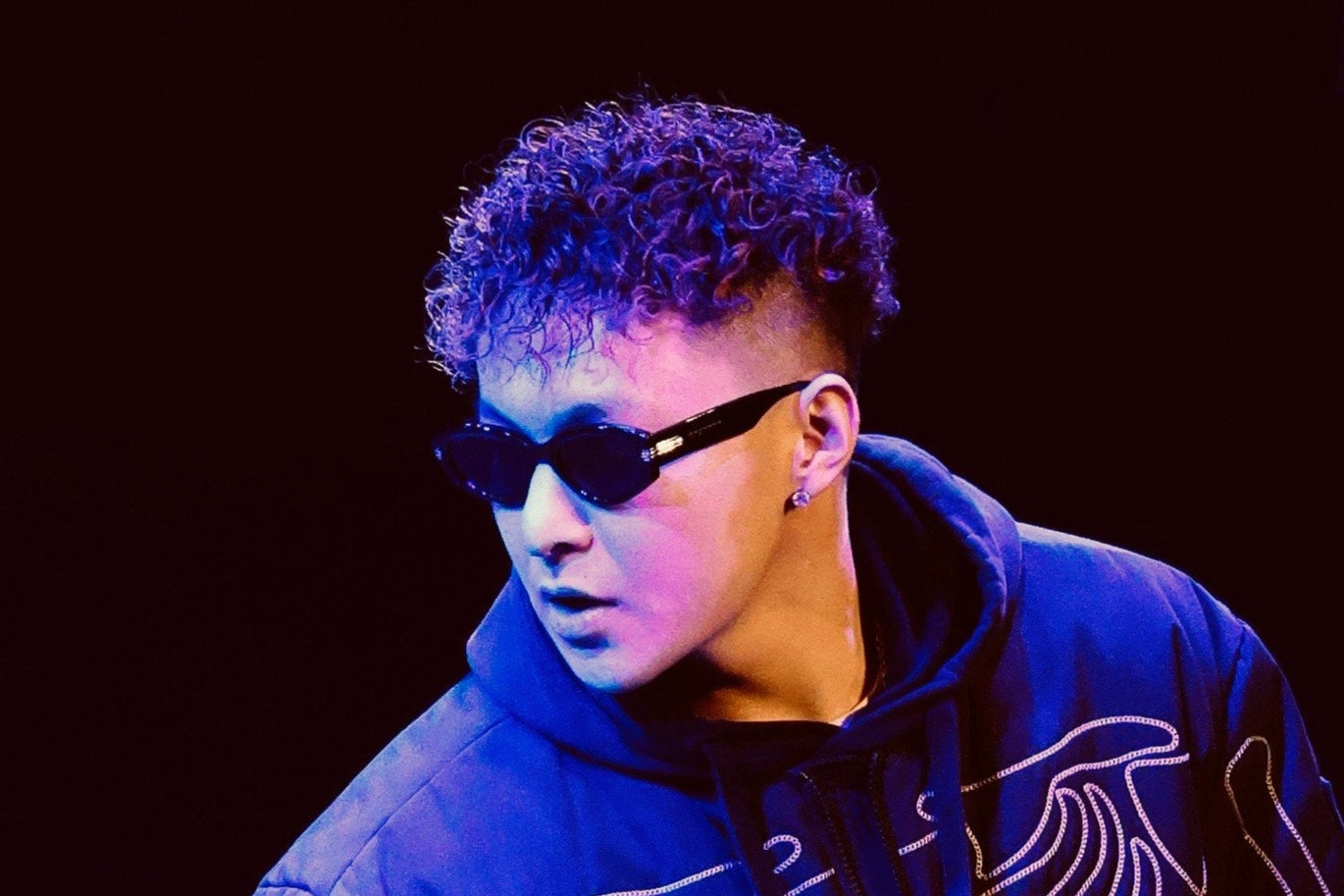 Person wearing a dark hoodie with a skeleton design on a stage-like setting